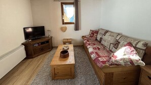 A cozy living room with a wooden ceiling, a television on a wooden stand, a sofa with patterned cushions, and a small table with a bowl. - Yéti 6 n° 8: renovated apartment at Petit Chatel (Châtel)
