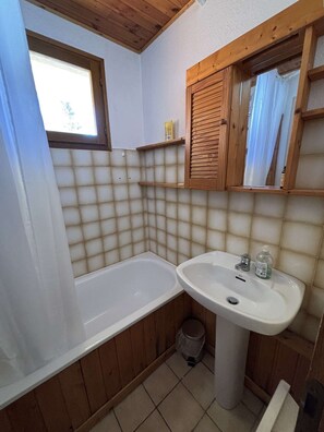 Une salle de bain avec une baignoire, un lavabo, des étagères en bois et une fenêtre.
