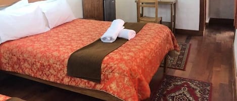 A hotel room with a bed, a desk, a chair, a TV, and a small table with flowers.