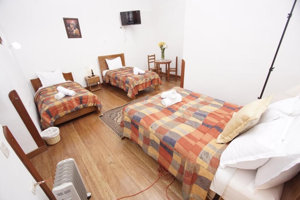 A hotel room with two beds, a TV, a small table with a vase, and a heater.