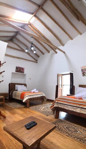 Un dormitorio con techo inclinado, vigas de madera, una cama con colcha estampada, una mesita de noche y un control remoto sobre una pequeña mesa.