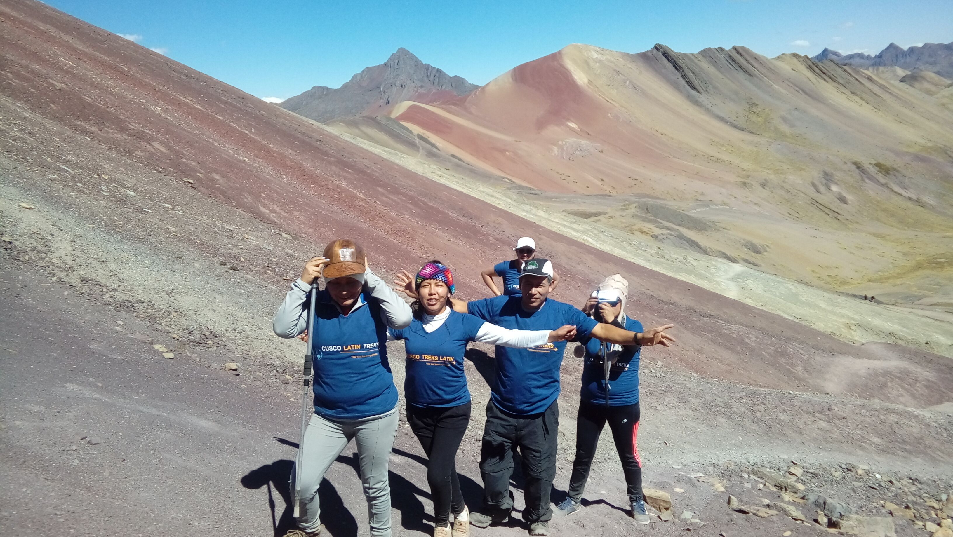 A group of people in blue shirts posing on a rocky mountain path with a clear sky.