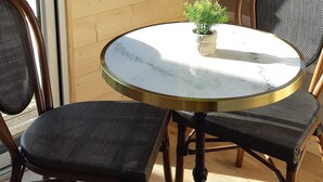 Ein runder Tisch mit Marmorplatte, umgeben von zwei Korbstühlen mit Metallbeinen. Auf dem Tisch steht eine kleine Topfpflanze.