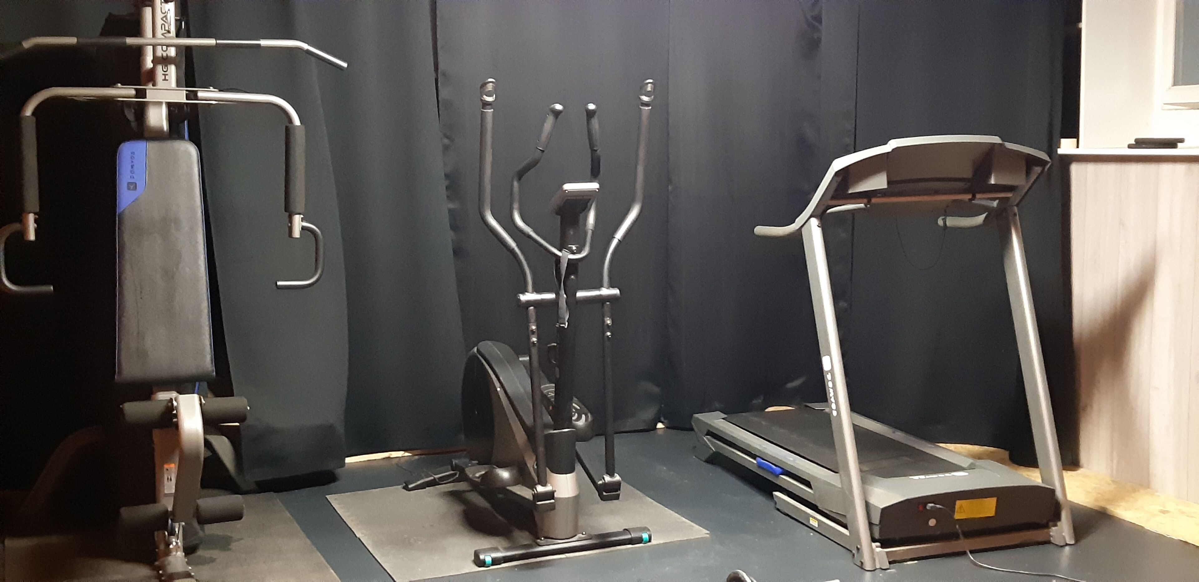 A gym with a treadmill, elliptical, and weight machine.