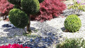 Un jardín con setos esféricos, arbustos de flores rojas y un sendero de grava.