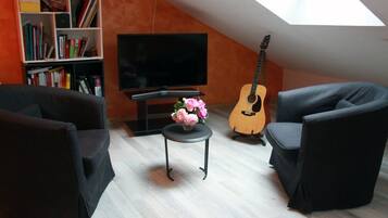 A living room with a flat-screen TV, a guitar, a bookshelf, and a small table with flowers.