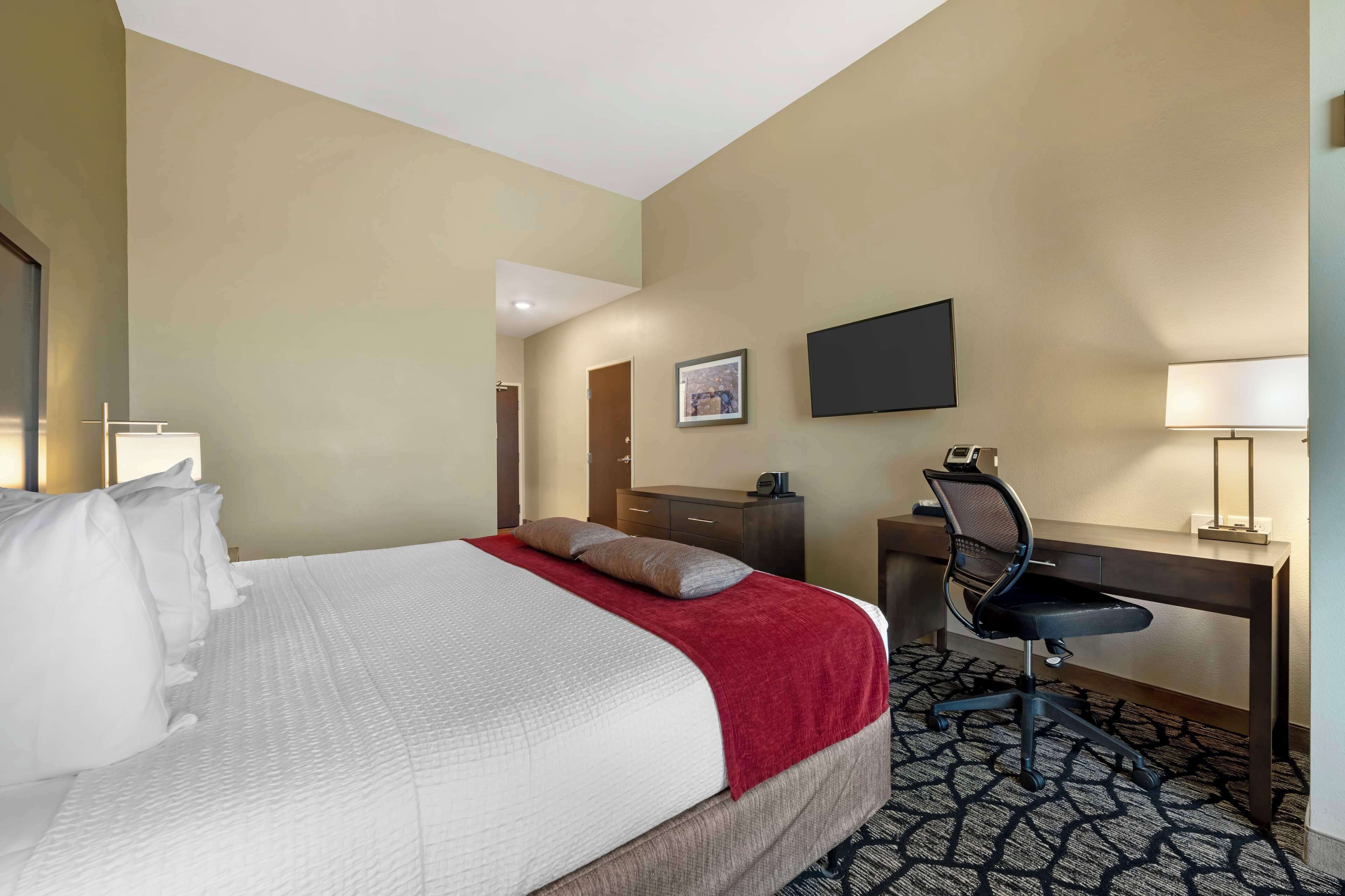 A hotel room with a bed, desk, chair, and a TV on the wall.