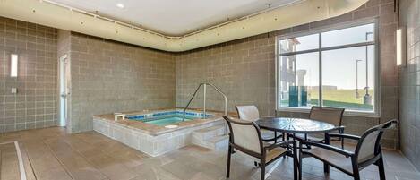 A spacious indoor area with a hot tub, a dining table with chairs, and a large window providing a view of the outdoors.
