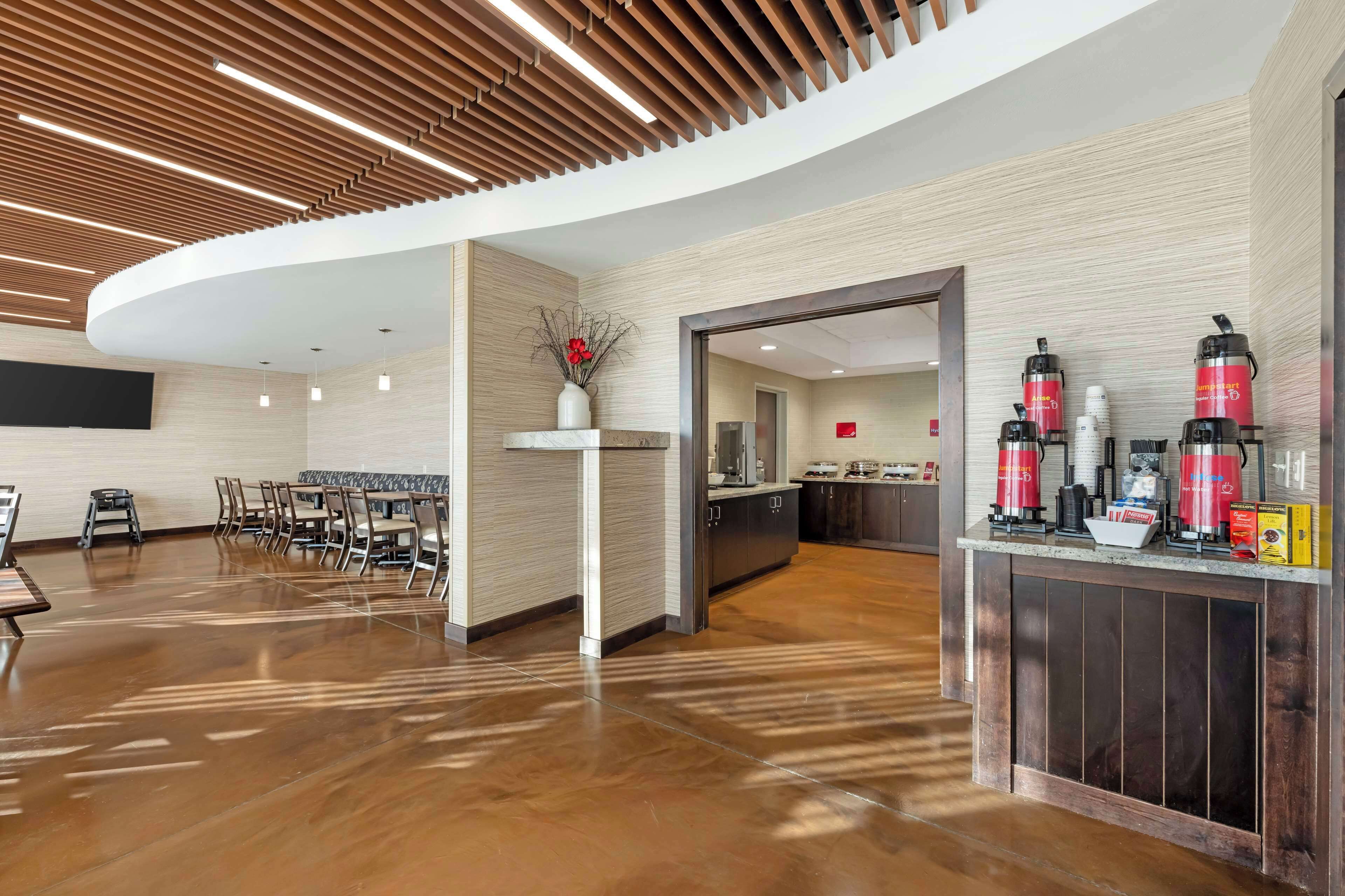 A modern hotel lobby with a curved reception desk, seating area, and a kitchen visible through an open doorway.
