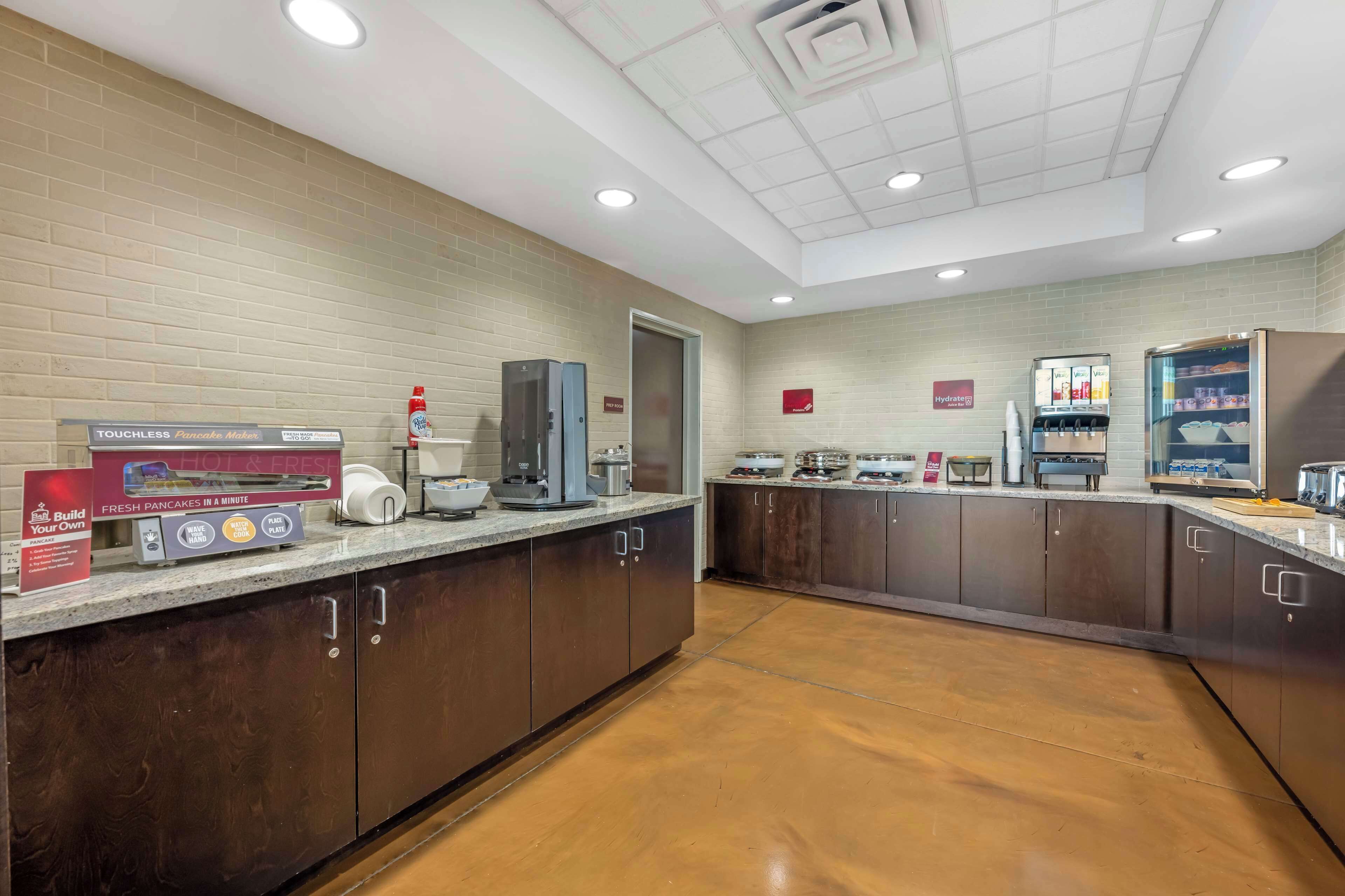 Una cocina moderna con un dispensador automático de panqueques, una cafetera y una estación de autoservicio para bebidas.