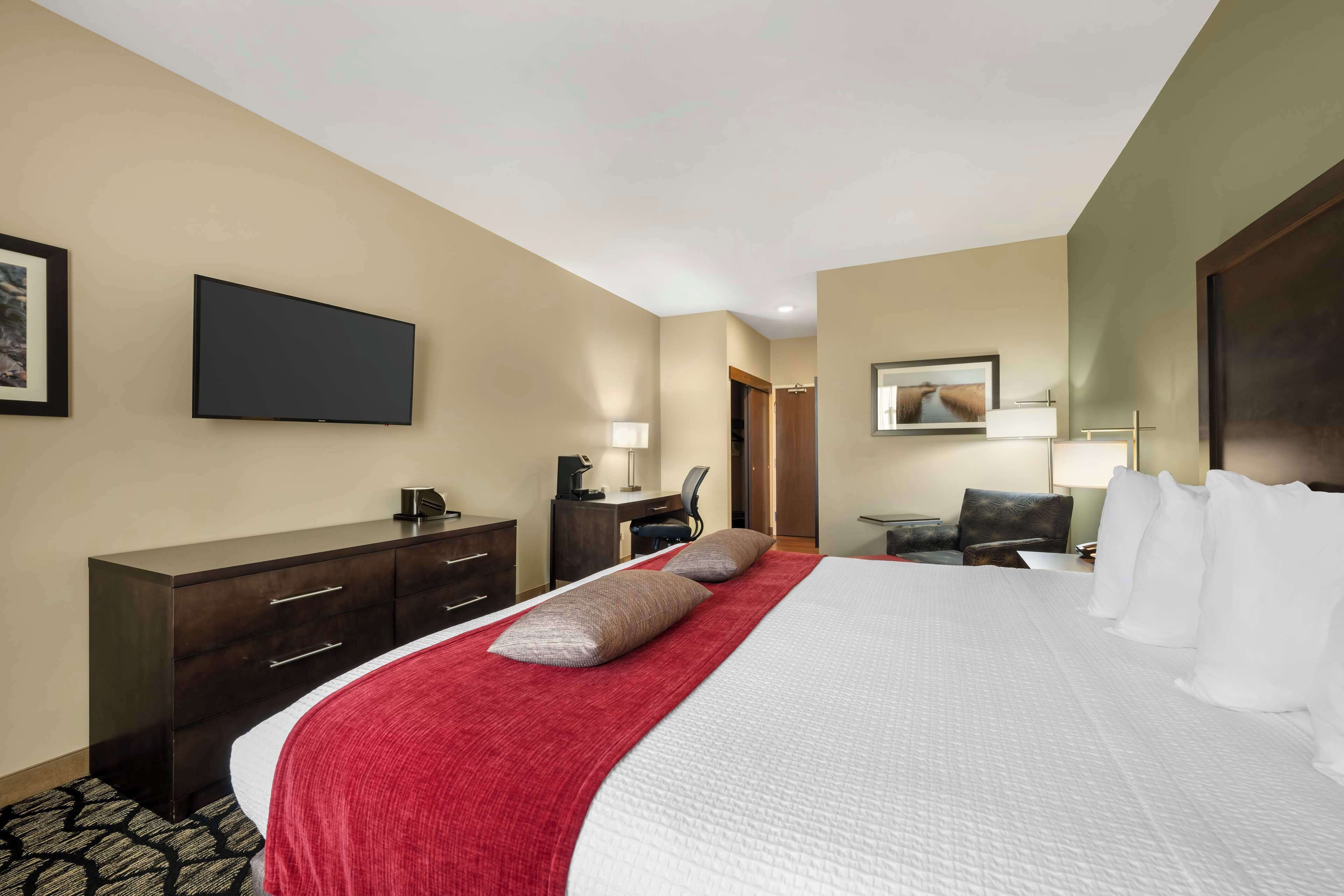 Habitación de hotel con una cama grande, un escritorio con una silla, un televisor de pantalla plana y una puerta que da a otra habitación.