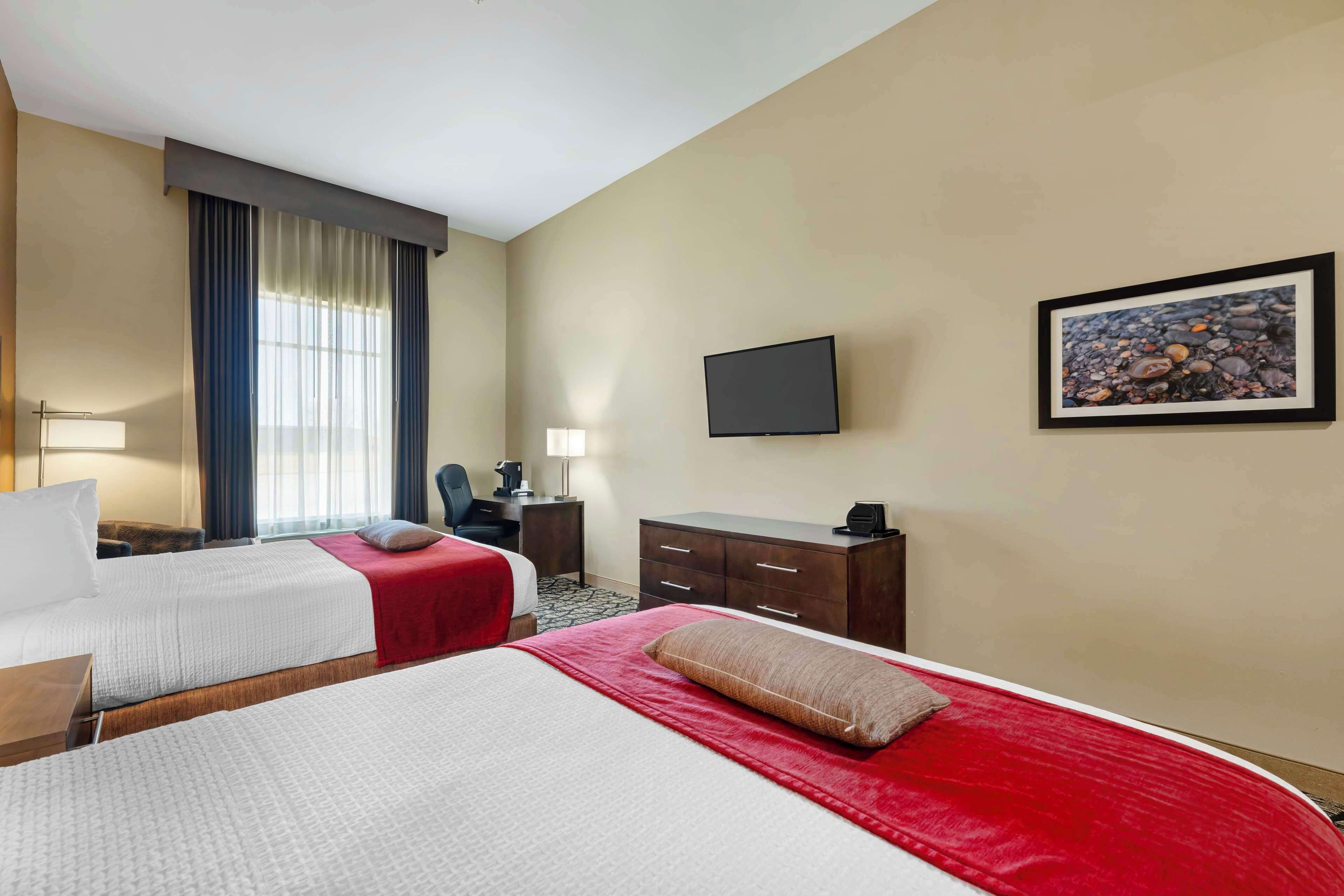 A hotel room with two beds, a TV, a desk, a chair, and a window with curtains.