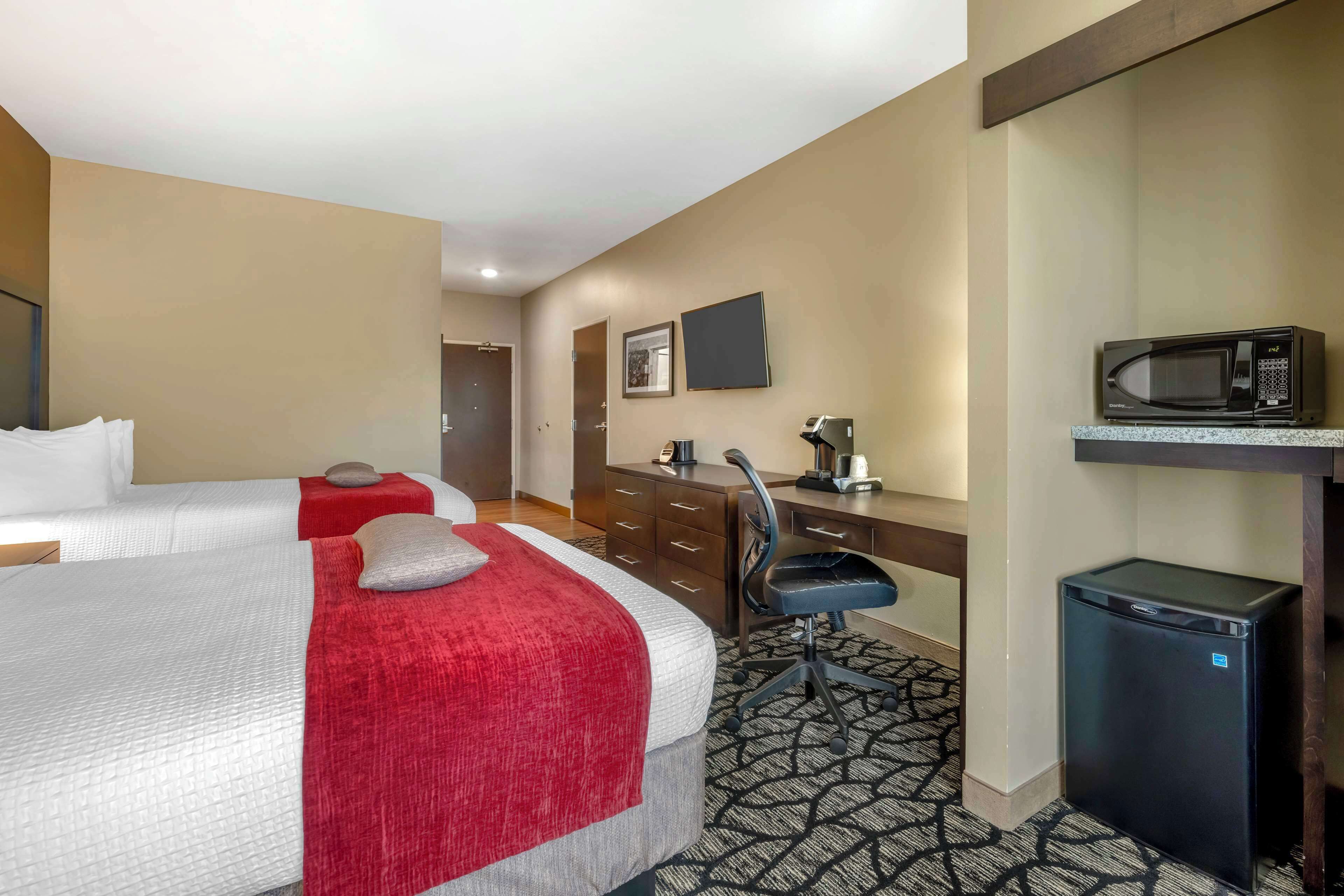 Une chambre d’hôtel avec deux lits, un bureau avec une chaise, un four à micro-ondes et un petit réfrigérateur.