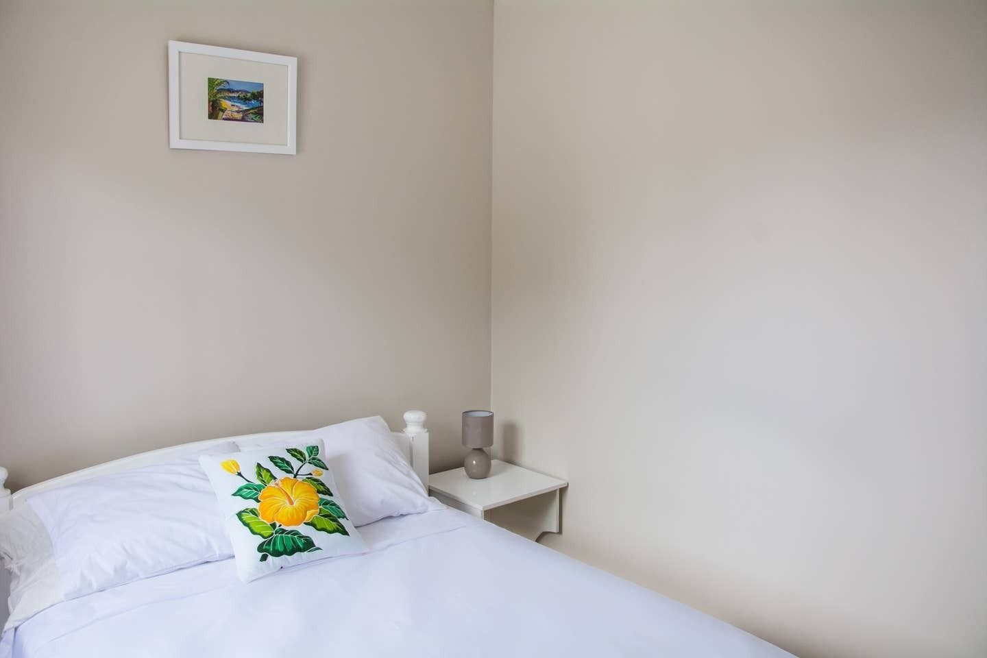 A bedroom with a bed, a bedside table, a lamp, and a framed picture on the wall.