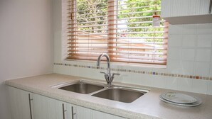 A kitchen with two stainless steel sinks, a window with blinds, and a tiled backsplash.
