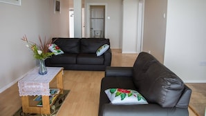 A living room with a black leather sofa, a small wooden table with a lace tablecloth, and a vase with flowers.