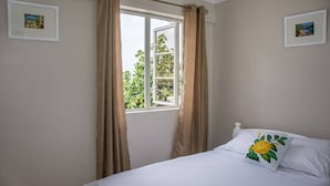 A bedroom with a bed, a window with curtains, and two framed pictures on the walls.