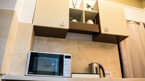 A compact kitchen with a microwave, a kettle, and a small shelf with decorative items. - ❤️ CityCenter Athenaeum Exquisite 1BD Apartment ❤️ (Sector 1)