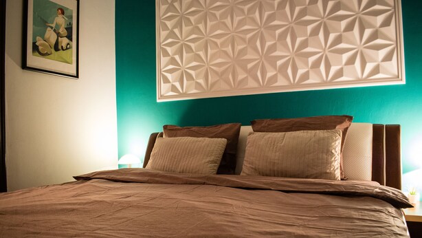 A neatly made bed with a brown bedspread and pillows, a geometric wall panel, and a framed picture on the wall. - ❤️ CityCenter Athenaeum Exquisite 1BD Apartment ❤️ (Sector 1)