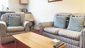 A living room with striped sofas and armchairs, a wooden coffee table, and a kitchen area in the background.