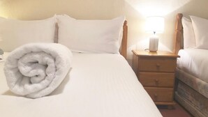 A neatly made bed with white linens, a rolled towel on the left side, and a bedside table with a lamp.