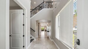 Un couloir avec un escalier, une porte et une fenêtre équipée de stores.