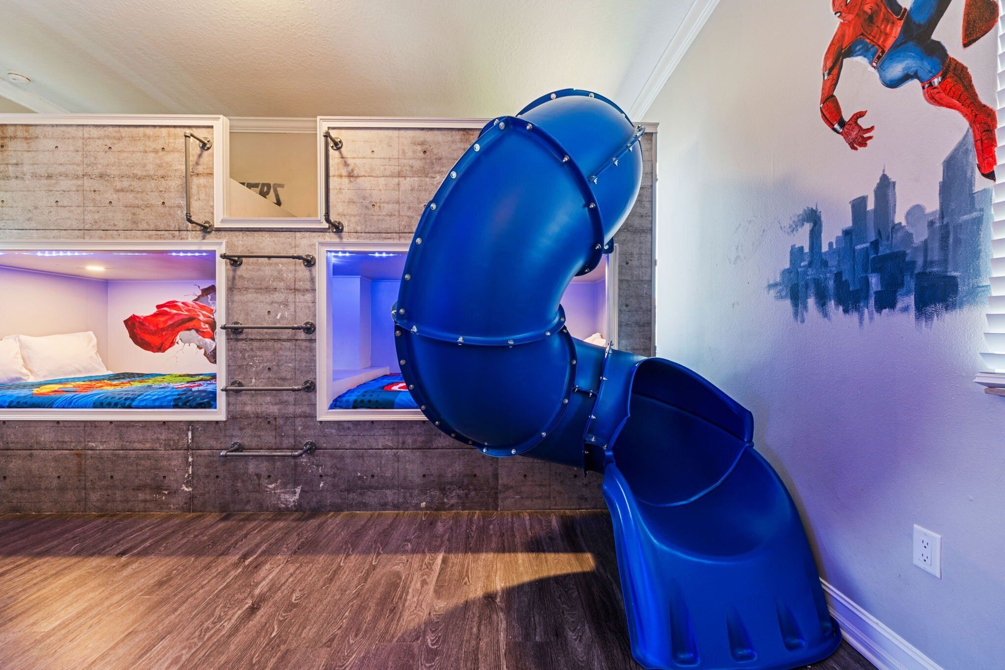 Une chambre avec des lits superposés, un toboggan et une fresque représentant Spiderman.