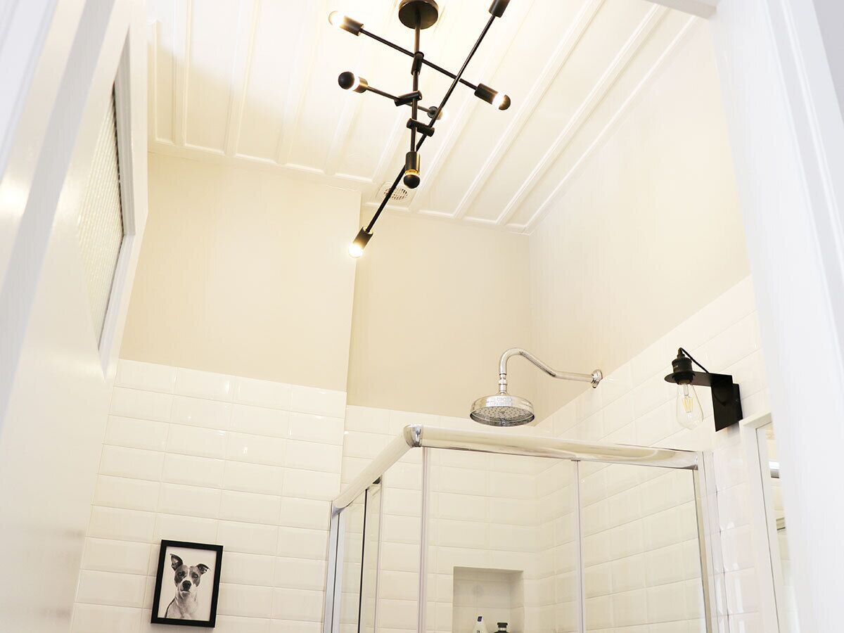Ein Badezimmer mit weißen Fliesen, einer Dusche mit Glastür und einer Deckenleuchte.