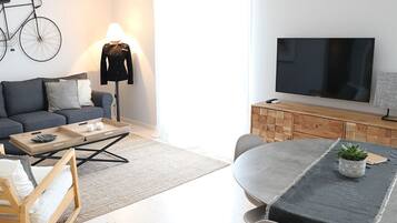 Ein modernes Wohnzimmer mit einer Couch, Couchtisch, Esstisch und einem Fernseher.