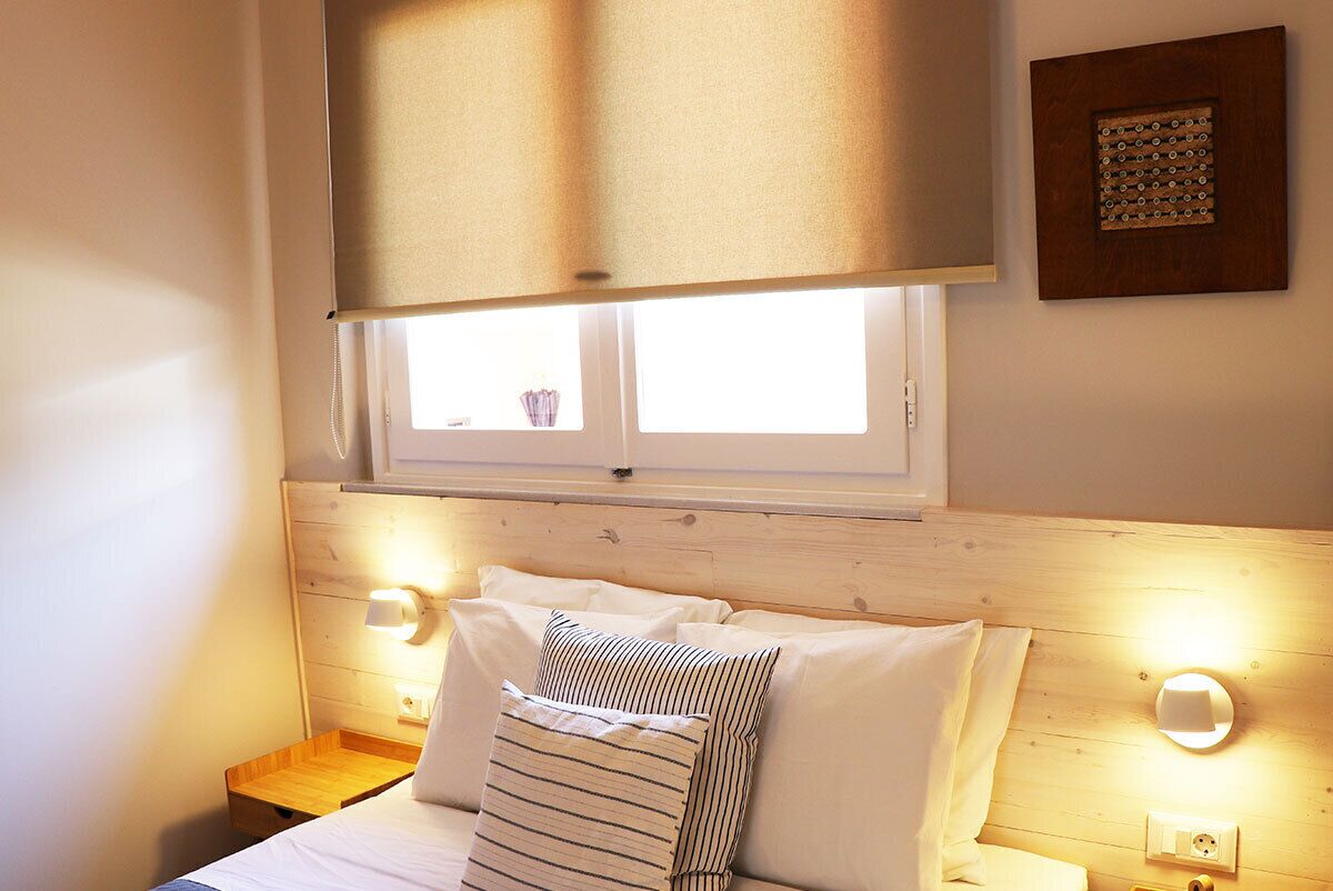 Ein Schlafzimmer mit einem Holz-Kopfteil, einem Fenster mit Jalousien, zwei Nachttischlampen und einem Nachttisch.