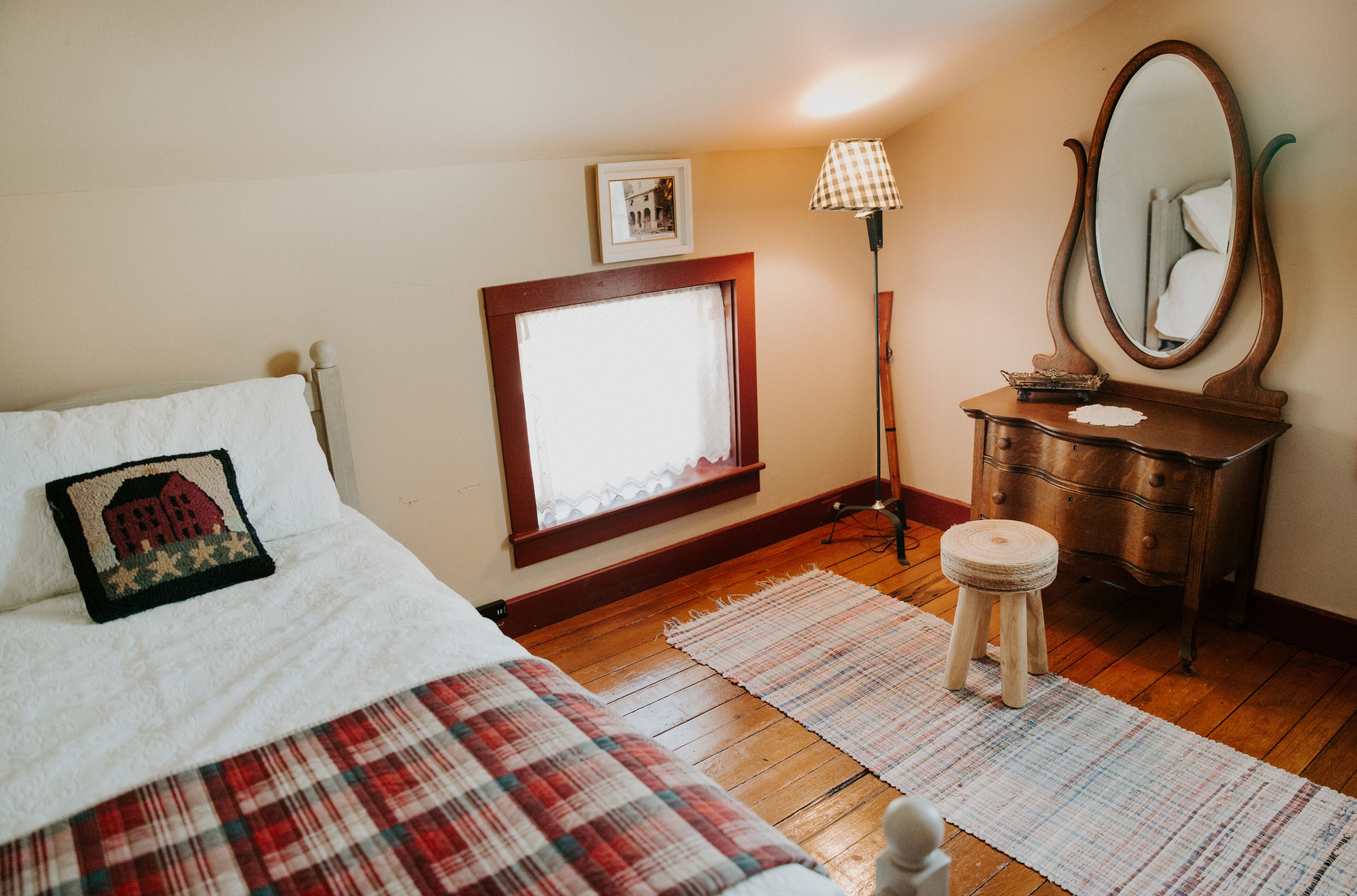 Ein Schlafzimmer mit Bett, Kommode, Spiegel, Fenster mit Vorhängen und Teppich.