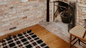 Une pièce rustique avec des murs en briques apparentes, un plancher en bois, une cheminée, une fenêtre avec un rideau et une chaise en bois.