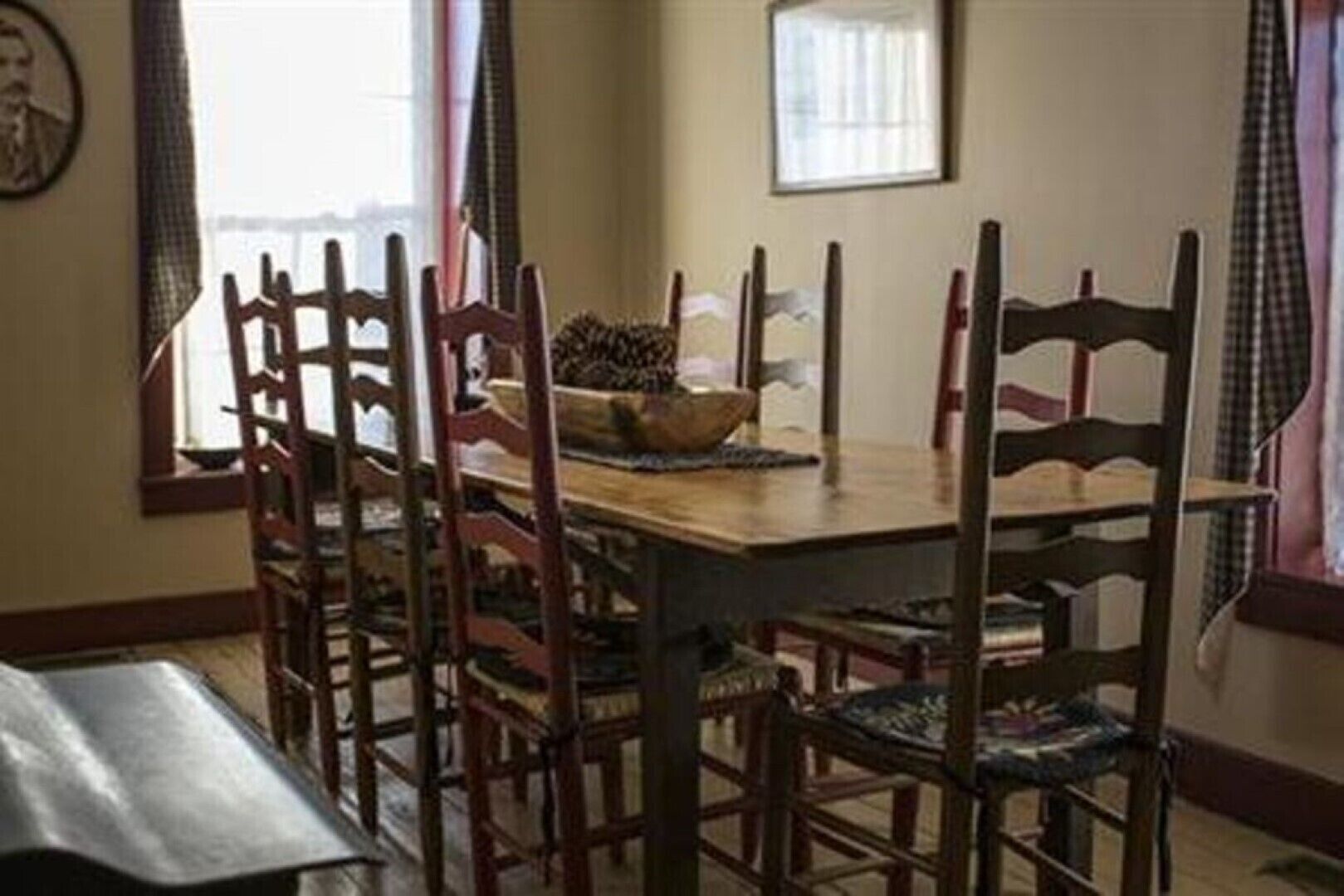 A dining area with a wooden table and chairs, a bowl on the table, and curtains on the windows.