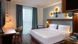 Une chambre d’hôtel avec un grand lit, un bureau, une chaise, une télévision et un luminaire fixé au mur.