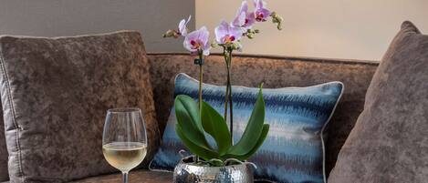 A modern living room with a sofa, a small round table, a glass of wine, and a decorative orchid plant.