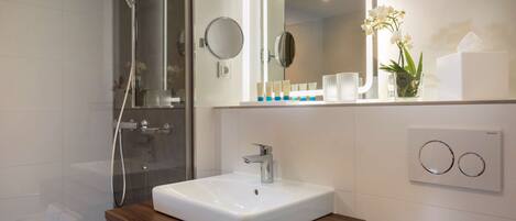 Un baño moderno con lavamanos blanco, tocador de madera y cabina de ducha de vidrio.