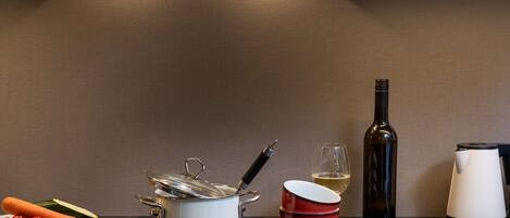 Una cocina moderna con una olla blanca sobre la encimera, un cuenco rojo, una botella de vino y una tetera.