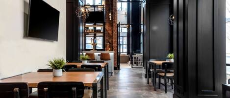 A modern restaurant interior with a long counter, multiple seating areas, and a large TV mounted on the wall.
