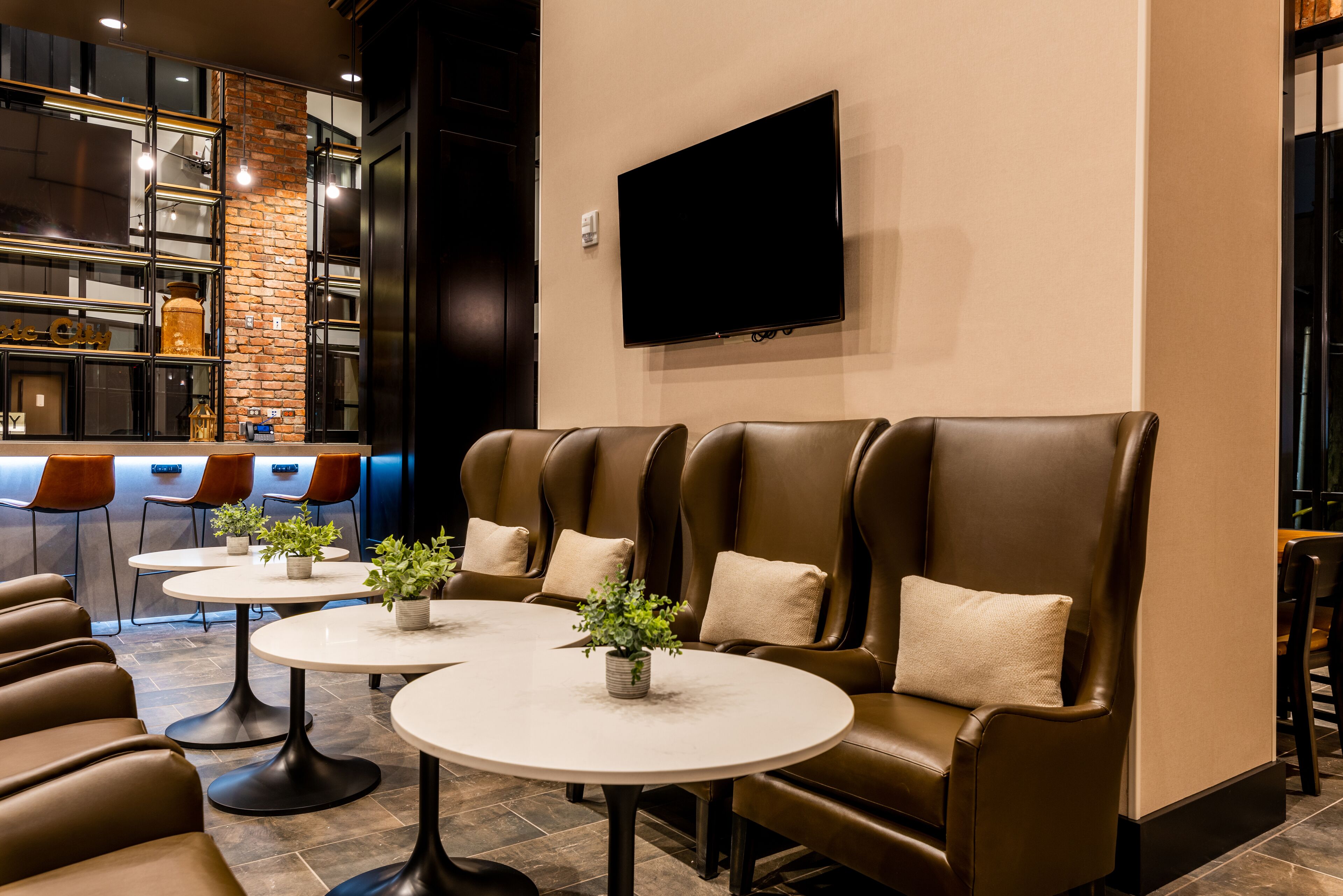 A modern lounge area with leather sofas, round tables, and potted plants.