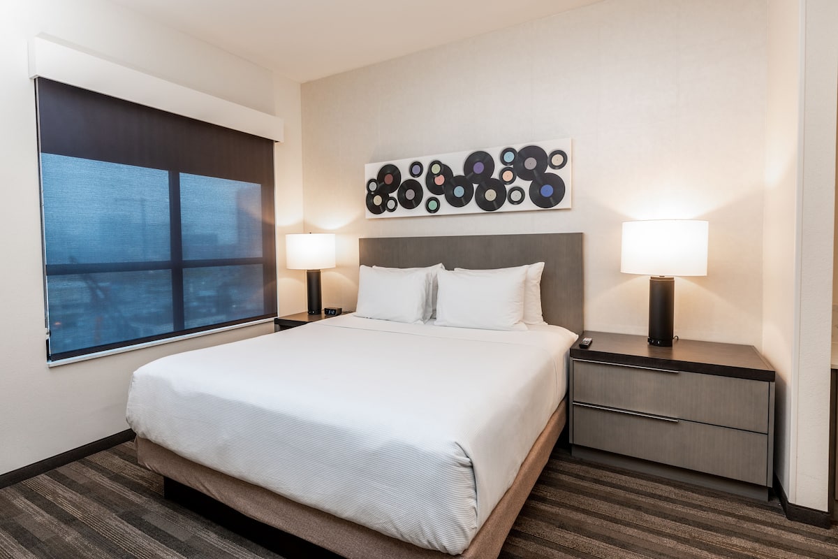 Ein Hotelzimmer mit einem großen Bett, zwei Nachttischen, einem Wandbild und einem Fenster.