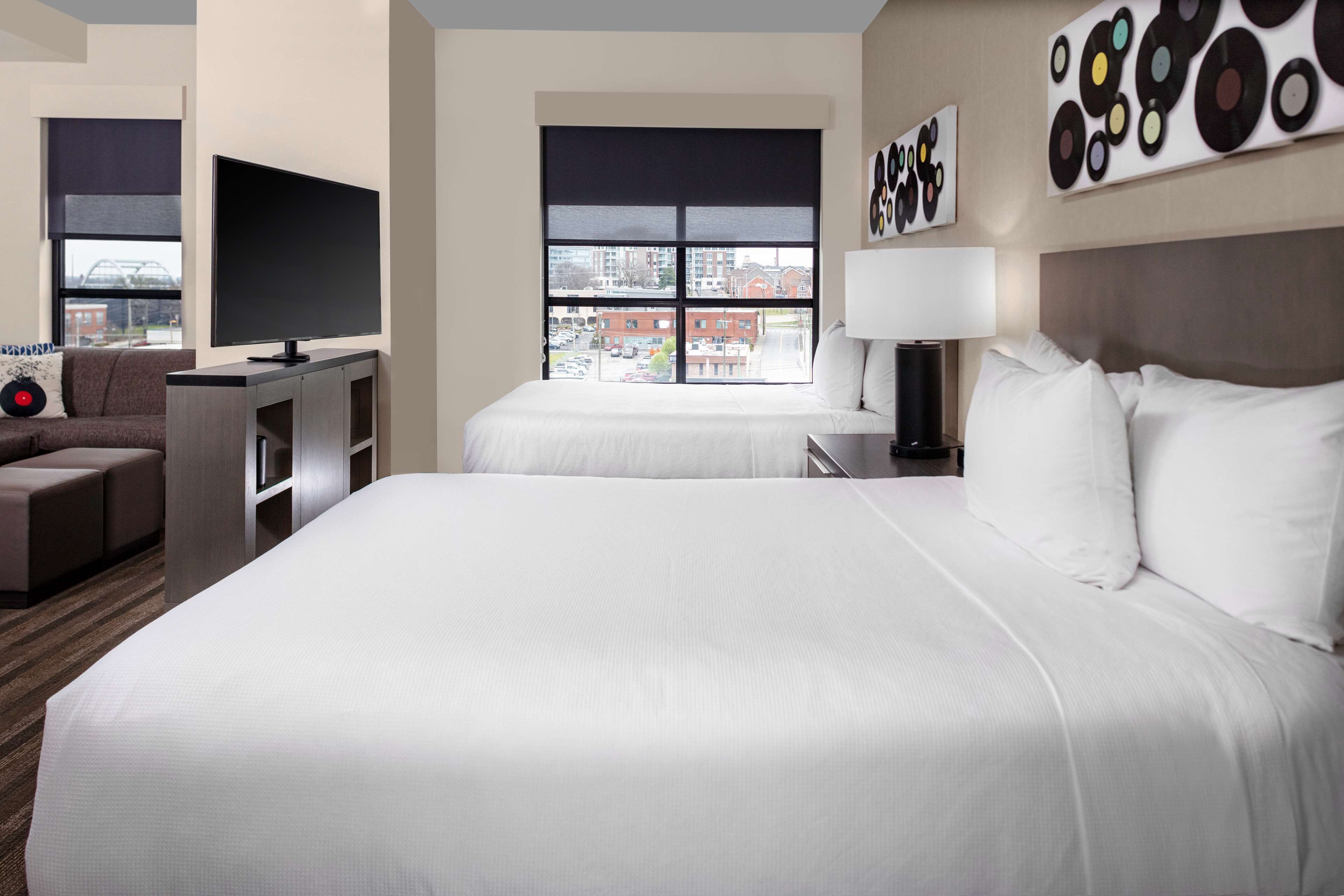 A hotel room with a large bed, a TV, a desk, and a sofa. There is a window with a city view.