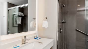 Un baño moderno con cabina de ducha de vidrio, un lavabo blanco con espejo y dos toallas colgadas en aros.