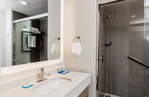 Un baño moderno con cabina de ducha de vidrio, un lavabo blanco con espejo y dos toallas colgadas en aros.