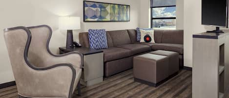 A modern hotel room with a sofa, a chair, a TV, and a painting on the wall.