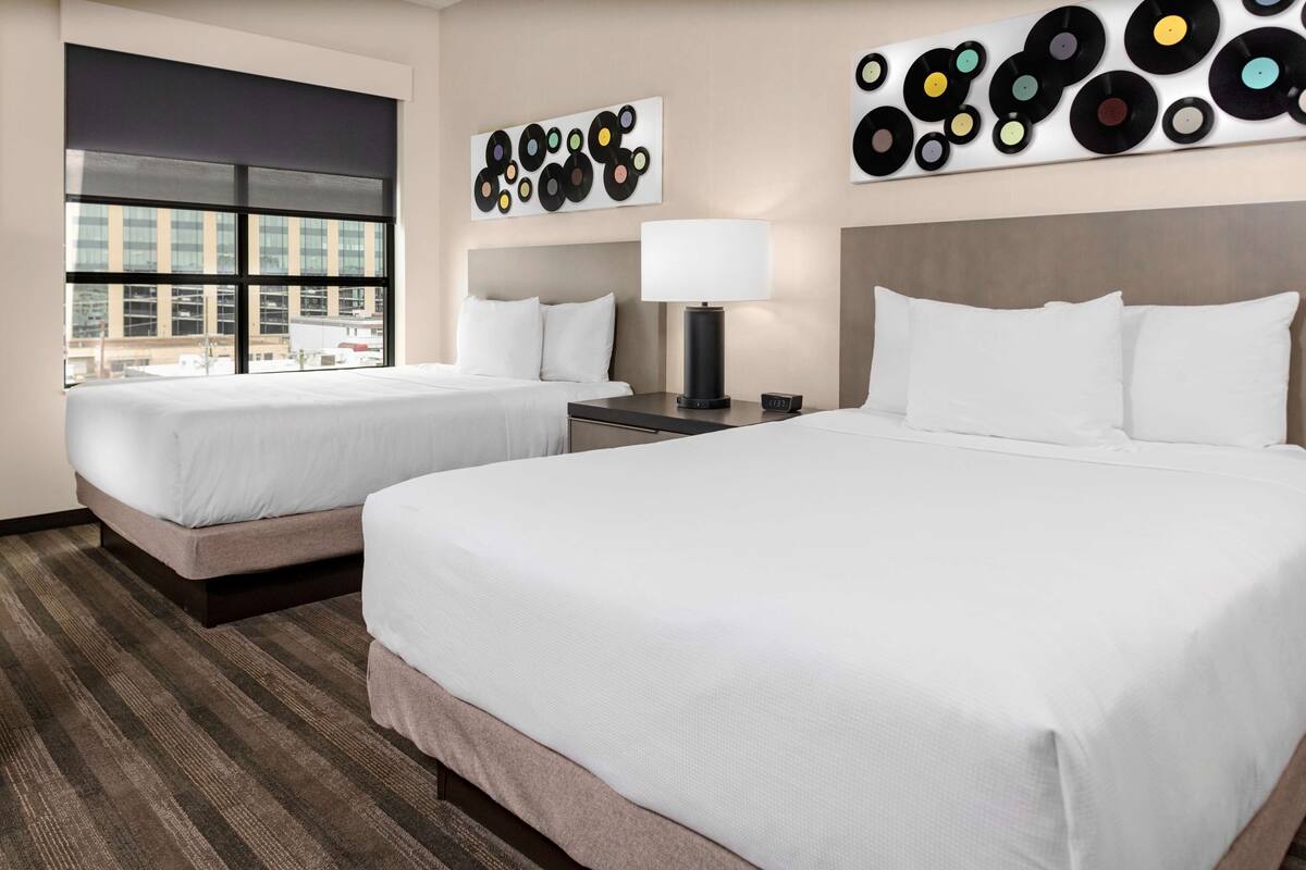 Ein Hotelzimmer mit zwei Betten, einem großen Fenster und einer Wand mit Wandgemälde im Stil von Schallplatten.