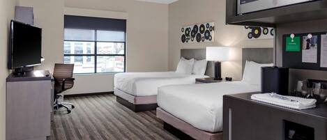 A hotel room with two beds, a desk, a television, a microwave, and a window with a city view.
