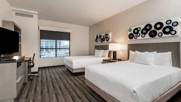 Habitación de hotel con dos camas, un escritorio, un televisor y vistas a la ciudad.