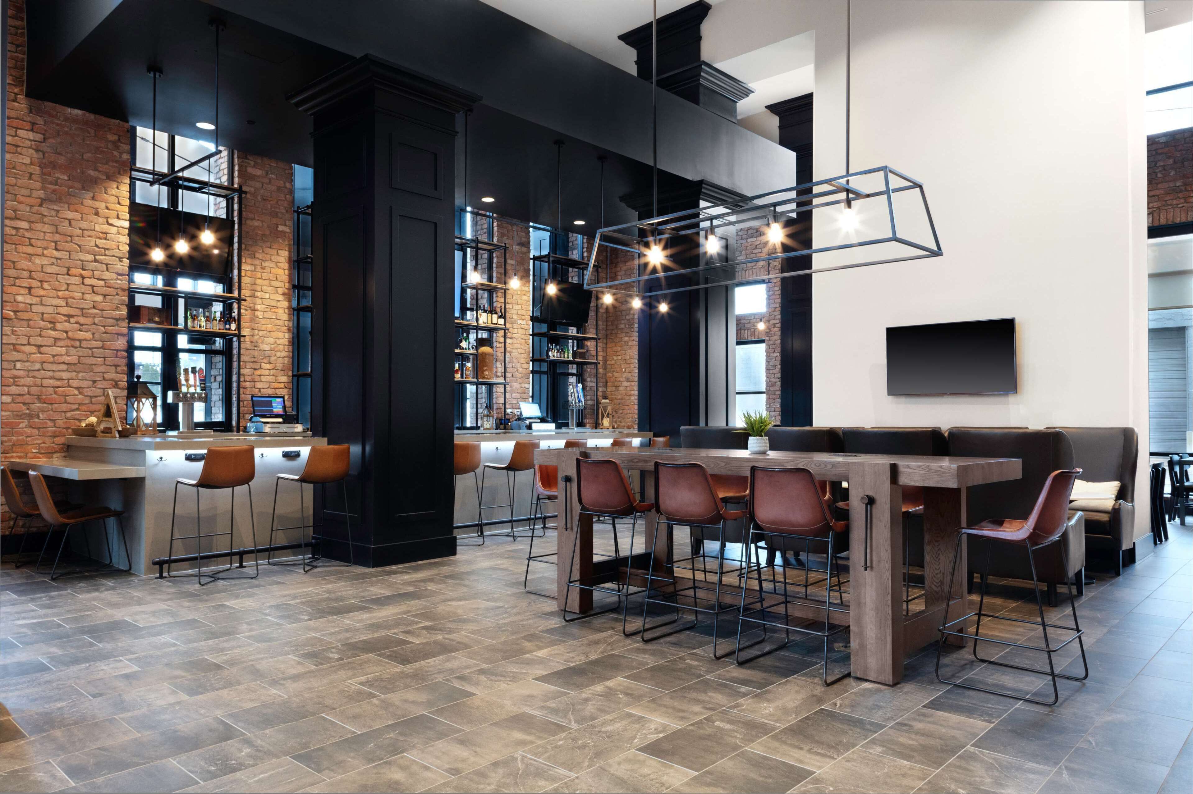 Eine moderne Bar mit Backsteinwand, Barhocker, einem Holzbalken als Tresen und Pendelleuchten.
