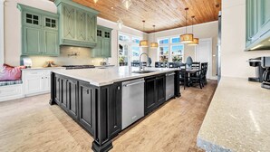 Una cocina amplia con una isla grande, armarios verdes y techo de madera.