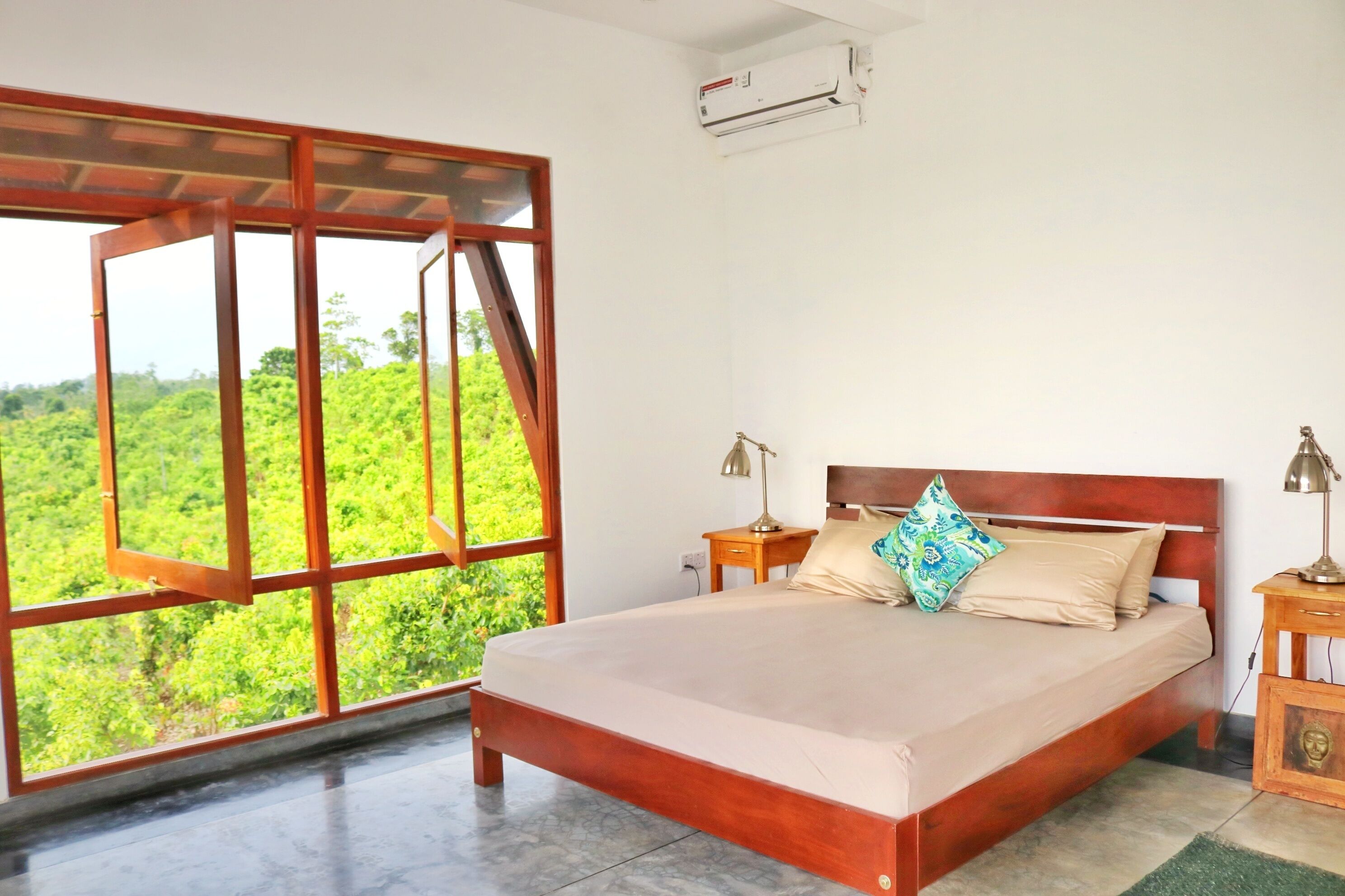 A bedroom with a large window, a bed, two bedside tables with lamps, and an air conditioning unit.